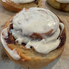 Load image into Gallery viewer, Cinnamon roll with cream cheese frosting on a light surface